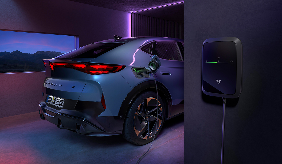 CUPRA Tavascan von hinten in einer Garage beim Laden an einer CUPRA Wallbox, violette Beleuchtung durch Fenster mit Berglandschaft.